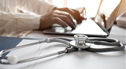 hospital records and stethoscope next to a doctor typing on a laptop 