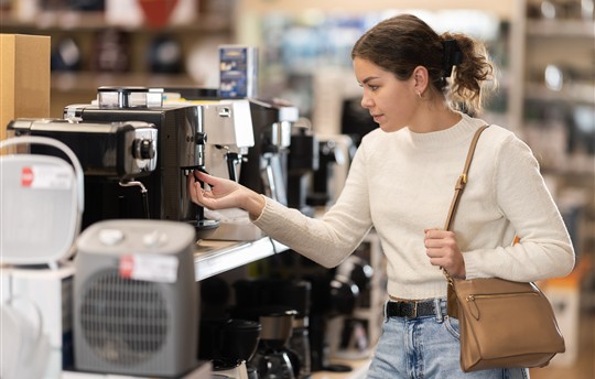 Young woman buyer chooses electric coffee machine in home appliance store