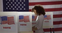 Profile, medium shot, young woman in polling station, voting in a booth with US flag in back