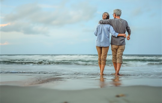 Senior couple walking on the beach holding hands at sunset